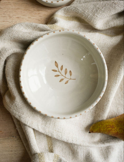 White ceramic bowl with leaf design on a beige cloth with pears