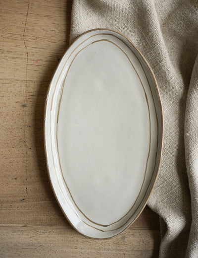 Oval ceramic plate with gold rim on a wooden surface with a beige cloth